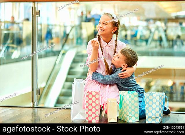 Junge umarmt seine Schwester im Einkaufszentrum zwischen vielen Einkaufstüten