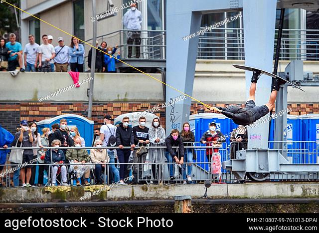 07 August 2021, Hamburg: A wakeboarder jumps through the air during a wakeboard event of the Austrian beverage company Red Bull in the Hafencity while the...
