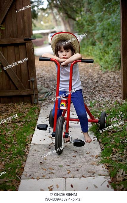 Portrait of four year old girl sitting on her tricycle in garden