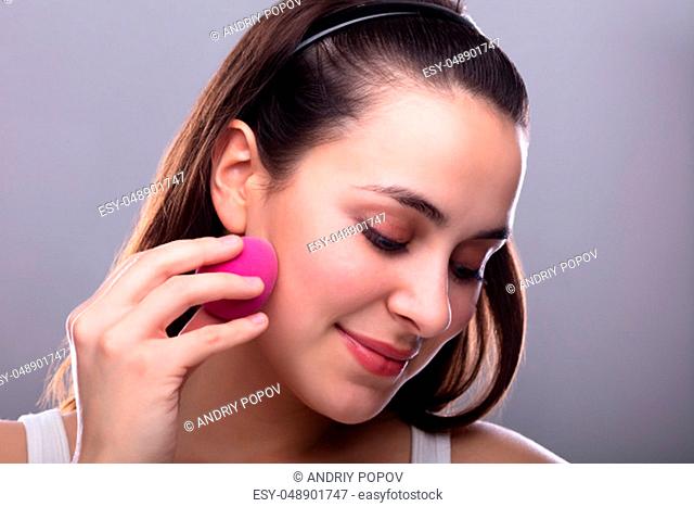 Beautiful Young Woman Applying Makeup Using Pink Blender Sponge