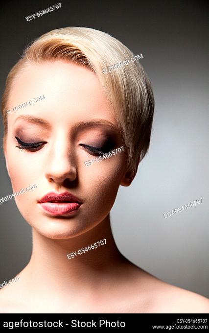 Close-up of young model with make-up, smooth skin and short blonde hair looking down.Studio shot