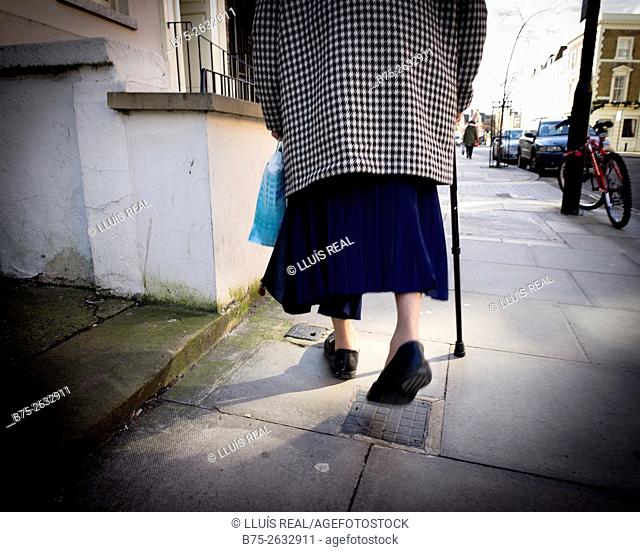 Closeup of the back view of an unrecognizable old lady, walking with stick in Stoke Newington Church Street, East London, England, UK, europe