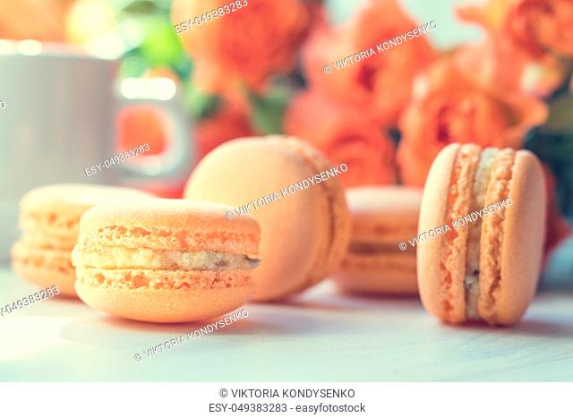 Orange mango or citrous macaroons and orange fresh little roses on light wooden background. Coloring and processing photo with light vintage style