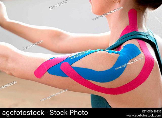 Closeup of a young fit womens shoulder with elastic therapeutic kinetic tape on her shoulder. Performing exercise at home