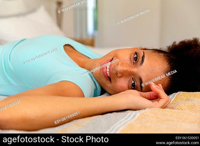 Mixed race woman lying in a bed looking at the camera and smiling