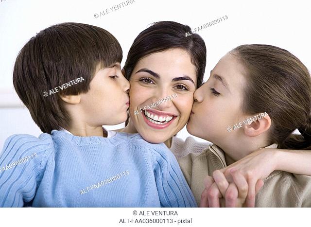 Portrait of smiling mother being kissed on each cheek by daughter and son