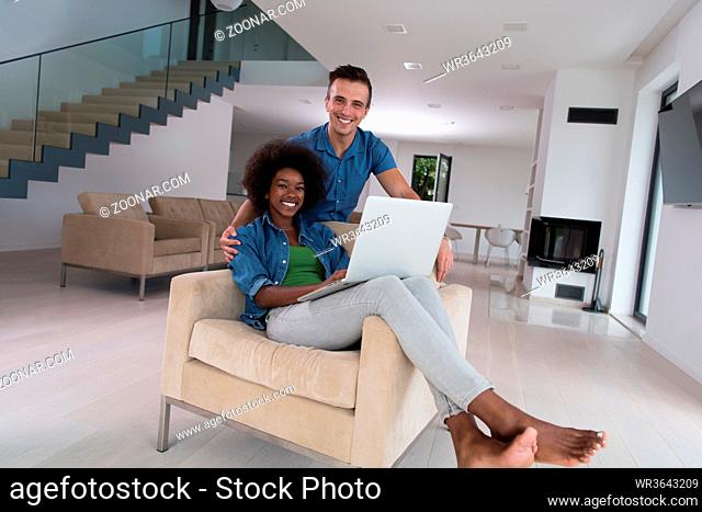 Young multiethnic couple sitting on an armchair in the luxury living room, using a laptop computer