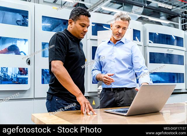 Businessman discussing over laptop with coworker in factory