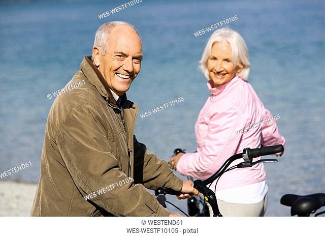 Germany, Bavaria, Walchensee, Senior couple pushing bikes across lakeshore