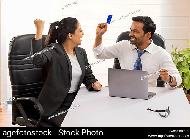 Happy business couple cheering with raising fists after successful transaction using credit card