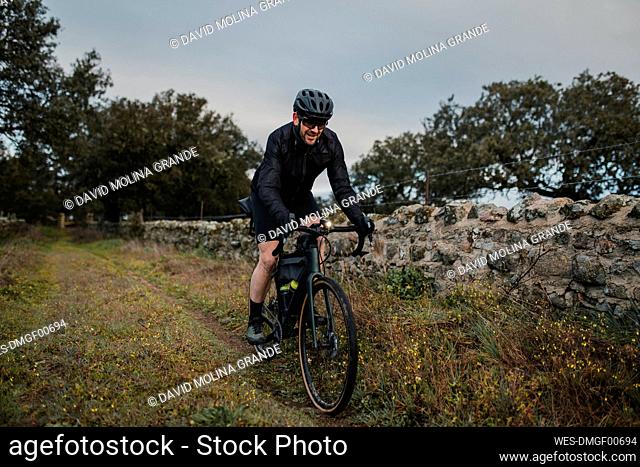 Smiling cyclist riding bicycle by wall