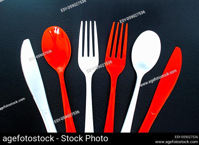 Single use red and white plastic cutlery on a leather background. Concept: Ban single use plastic