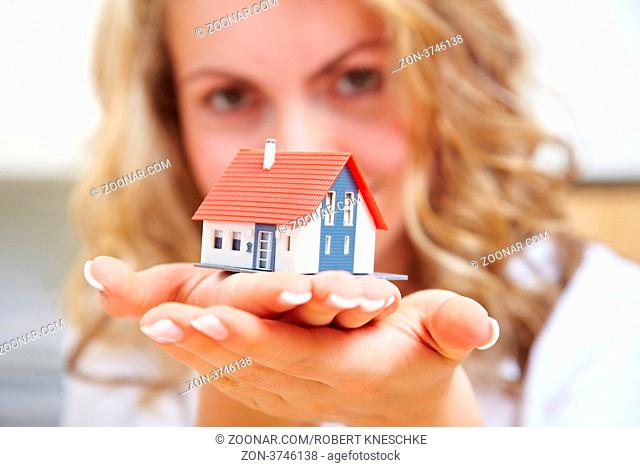 Frau trägt ein kleines Einfamilienhaus auf ihren Händen