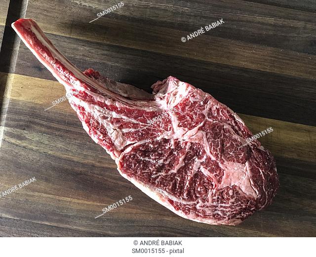 Close up of raw beef meat. Tomahawk ribeye steak, bone-in, on wooden cutting board