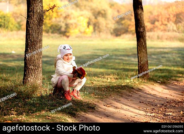 little cute baby girl with bouquet of yellow and red leaves in the forest on a sunny autumn day