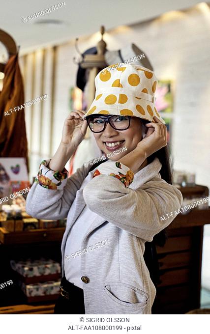 Young woman trying on hat in shop, portrait