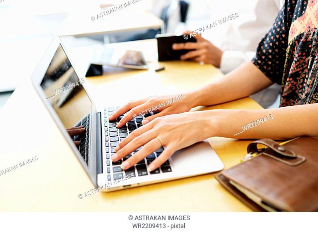 Cropped image of female student using laptop at desk in classroom