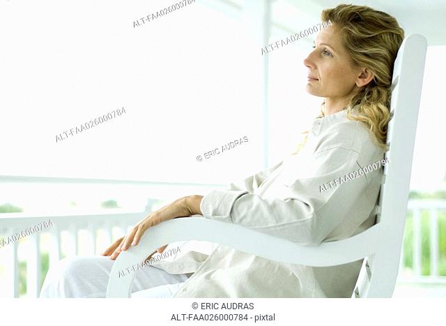 Woman sitting in rocking chair on porch, side view