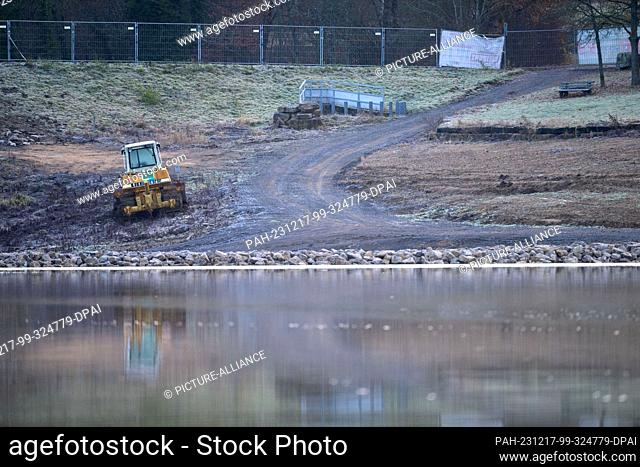 PRODUCTION - 15 December 2023, Bavaria, Stadtlauringen: An excavator stands at the edge of Lake Ellertshausen, with a new dam stretching through the main lake...