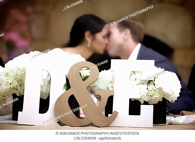 Bride and groom kissing at their reception behind big initial signs at their sweetheart table