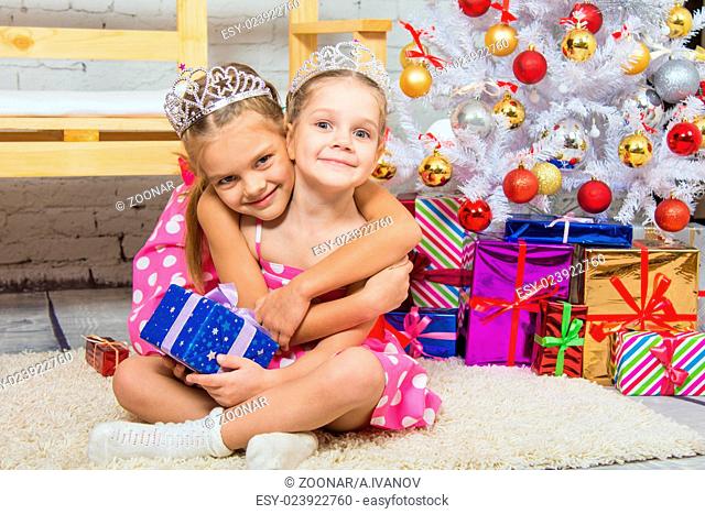 Girl hugging another girl sitting on a mat at the Christmas tree