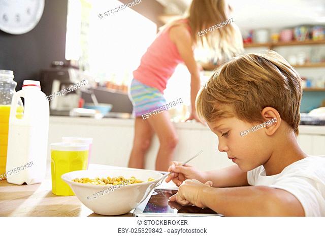 Children Eating Breakfast And Playing With Digital Tablet