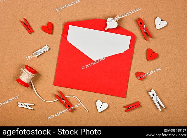 Packing Valentine card envelope with twine, clothespins and hearts over brown paper background, close up flat lay, elevated top view, directly above