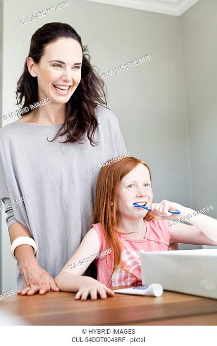 Mother watching daughter brush teeth