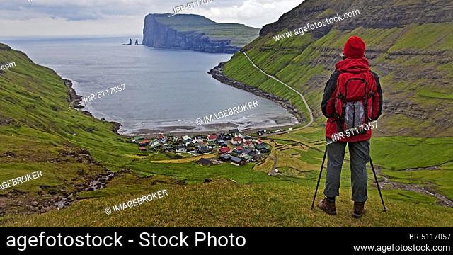 A hiker looks at the small village Tjørnuvík and the Atlantic Ocean, Streymoy, Faroe Islands, Føroyar, Denmark, Europe
