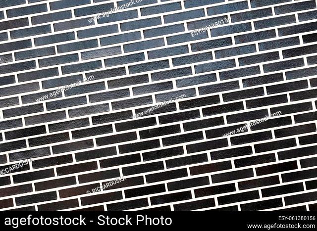 A black brick wall texture with white grout line, slanted plane. Abstract background with copy space