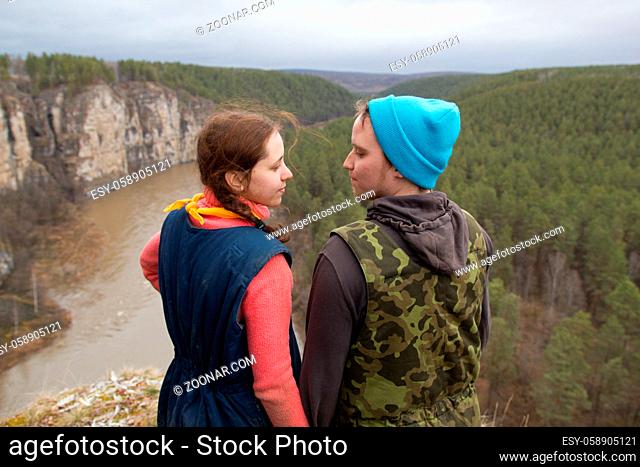 Young couple hikers standing on the edge of a cliff and holdind hands over the mountain river , telephoto shot