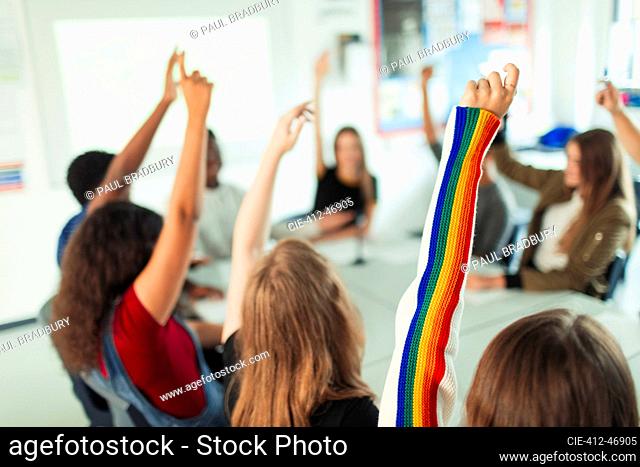 High school students with arms raised, asking questions in classroom