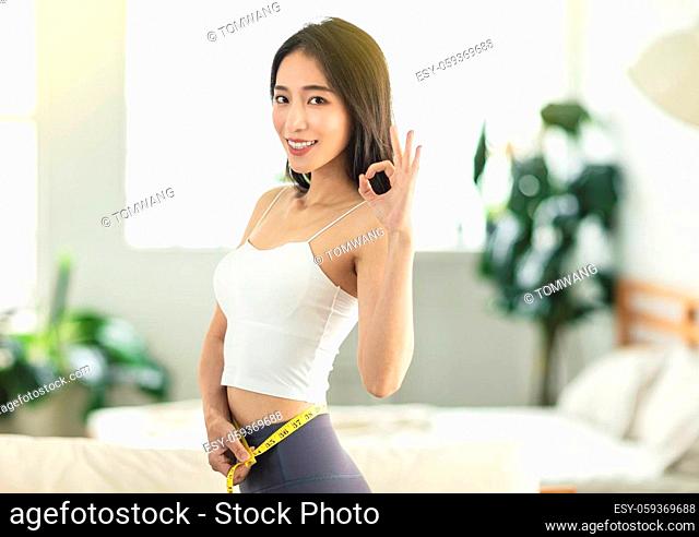 young woman holding a measuring ruler while dancing, turning around, very satisfied with her posture, very happy to lose weight, with an OK gesture