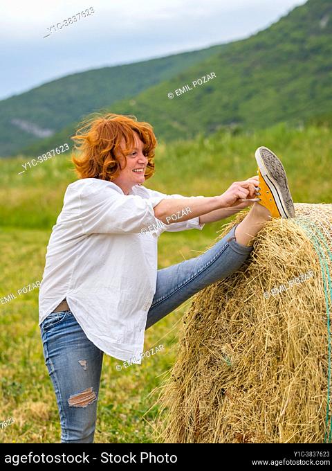 Mature woman raised leg high on haystack tying laces smiling