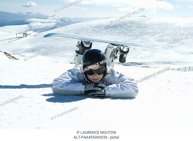 Young snowboarder lying on the ground, head resting on arms, smiling at camera