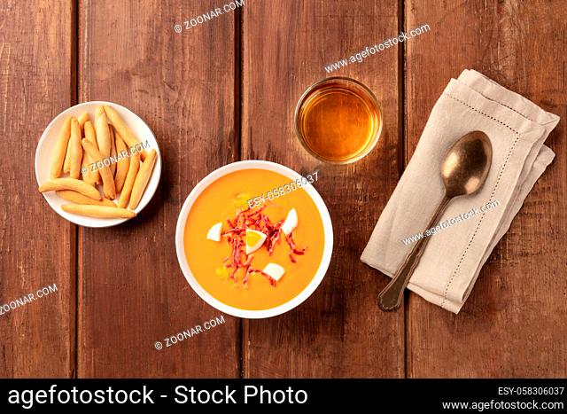 Salmorejo, Spanish cold tomato soup, overhead shot on a dark rustic wooden background with wine and picos, typical breadsticks