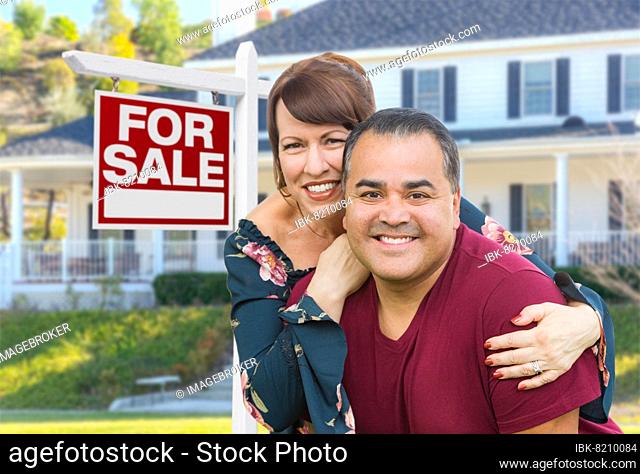mixed-race young adult couple in front of house and for sale real estate sign