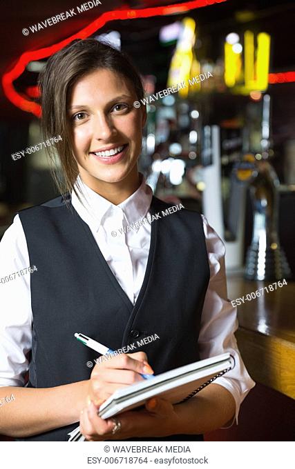 Happy barmaid smiling at camera taking notes