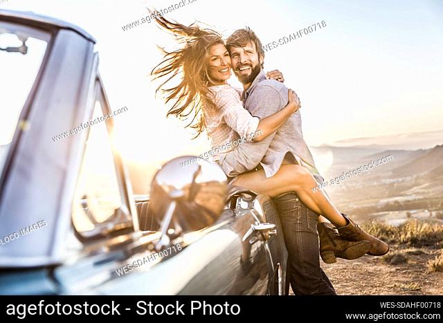 Happy couple at convertible car in the countryside at sunset