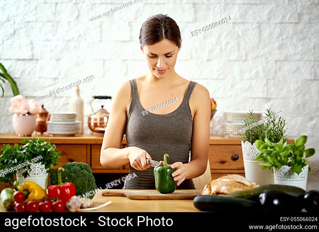 beautiful young woman, brunette cutting green peppers in the kitchen on a table full of organic vegetables