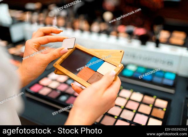 Woman holds eyeshadows at the shelf in cosmetics store. Buyer at the showcase in luxury beauty shop salon, female customer in fashion market