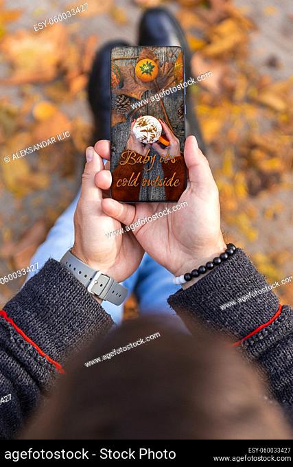 Man received love photo message invitation for coffee on smartphone while sitting outdoors in a park full of autumn leaves on the ground