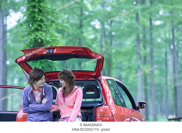 Young Couple Sitting on Vehicle Trunk and Chatting