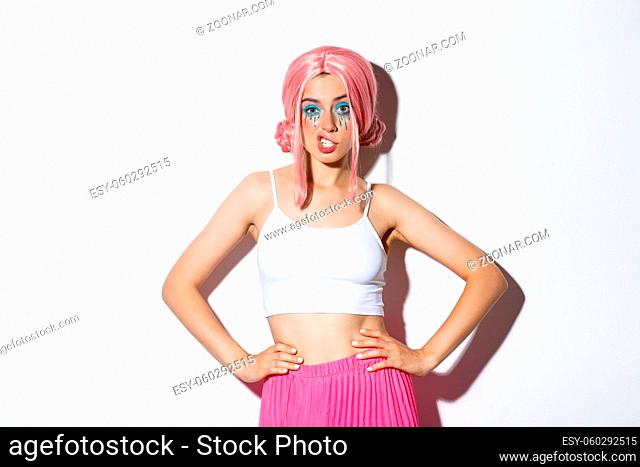 Portrait of sassy attractive woman with pink anime wig, bright makeup, showing teeth and looking confident, celebrating halloween