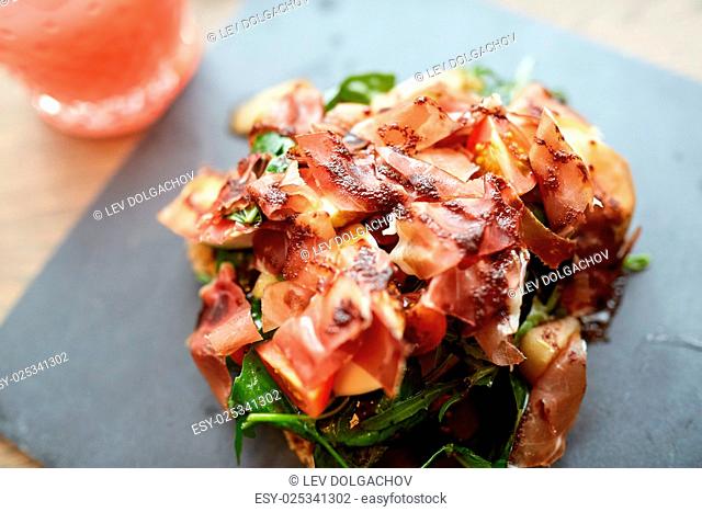 food, dinner, haute cuisine and eating concept - prosciutto ham salad on stone plate at restaurant