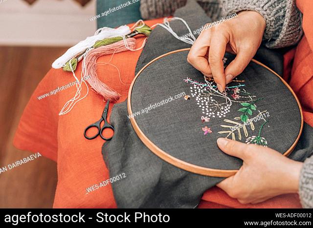 Hands of fashion designer doing embroidery on fabric with thread at workshop