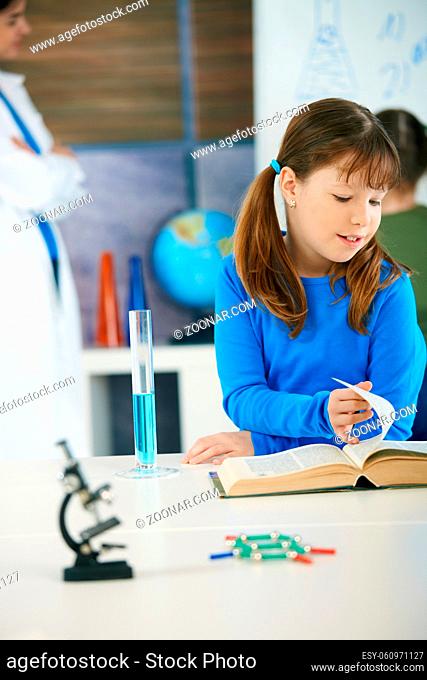 Elementary age schoolgirl looking at book in science class in primary school classroom