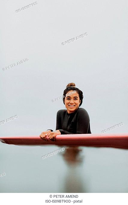 Young female surfer leaning on surfboard in calm misty sea, portrait, Ventura, California, USA