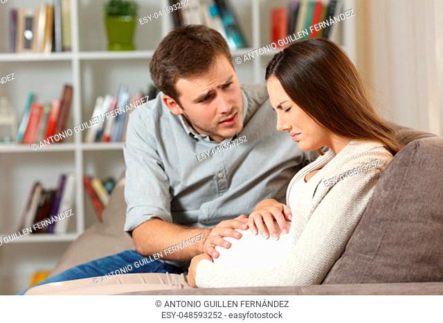 Pregnant woman suffering belly ache and husband comforting her seated on a sofa at home