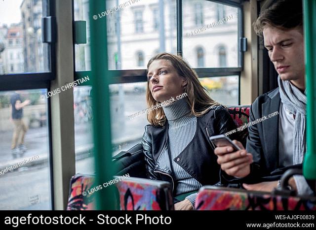 Thoughtful woman sitting with male colleague using smart phone in bus